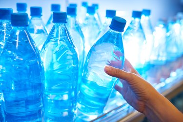 a close up of a person's hand reaching for a plastic bottle of water on a shelf