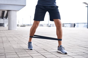 Close-up of young sportive man uses resistance band for exercising outdoors