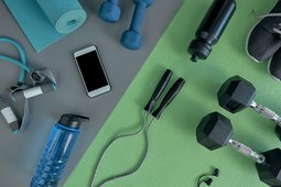 Top view of exercise equipment, including dumbbells, jump rope, resistance bands and green yoga mat