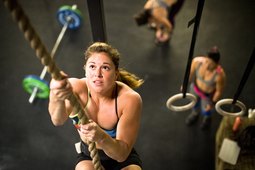 Female athlete performing rope climbing in CrossFit gym