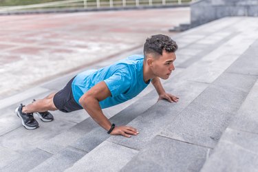 young guy, a male athlete, is wrung out in summer city, training muscles of chest and arms, active lifestyle, health and sport concept, full-length sportswear, fitness bracelet on his arm.