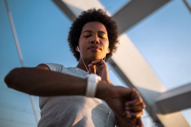 Fit person with short dark curly hair checking heart rate while exercising on both a watch and by taking their pulse