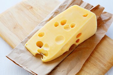 A wedge of Swiss cheese on a wooden cutting board