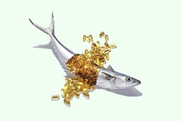 yellow Fish Oil capsules Bursting From a Whole Fresh Mackerel on a light green background