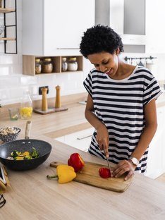 A woman cutting peppers as she follows a recipe on her kindle set up on a stand