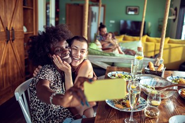 Two young adult friends taking a selfie around the dinner table, socializing as part of their New Years resolution.