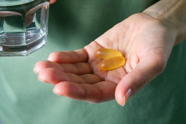 closeup of hand holding omega-3 fish oil capsules above a light green sink