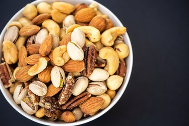 an overhead photo of mixed nuts in a white bowl on a black background