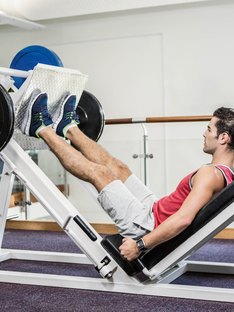 A young man doing leg presses on a squat machine at the gym