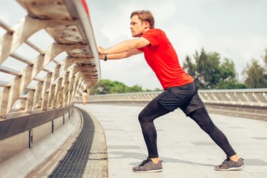 adult in a red shirt outside doing a standing calf stretch for the back of the knee