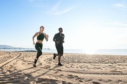 man and woman running on the beach with blue sky