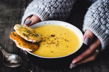 a close up of a person following a soup diet holding a bowl of yellow soup